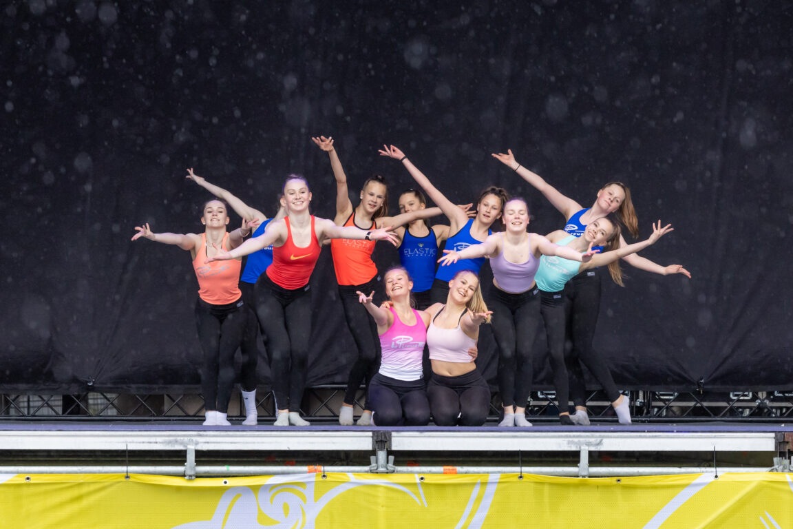 Nuoria värikkäissä topeissa ja leveät hymyt huulilla poseeraamassa lavalla kädet auki ylöspäin.