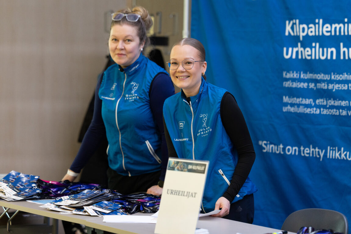 Seuratyöntekijät sinisissä liiveissä valmiina urheilijoiden ilmoittautumisessa