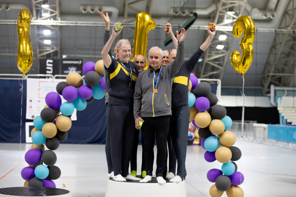 Kuopion Voimistelu-Veikot palkintopallilla. Kuusi ikämiestä, jotka vilkuttavat mitalit kaulassa.