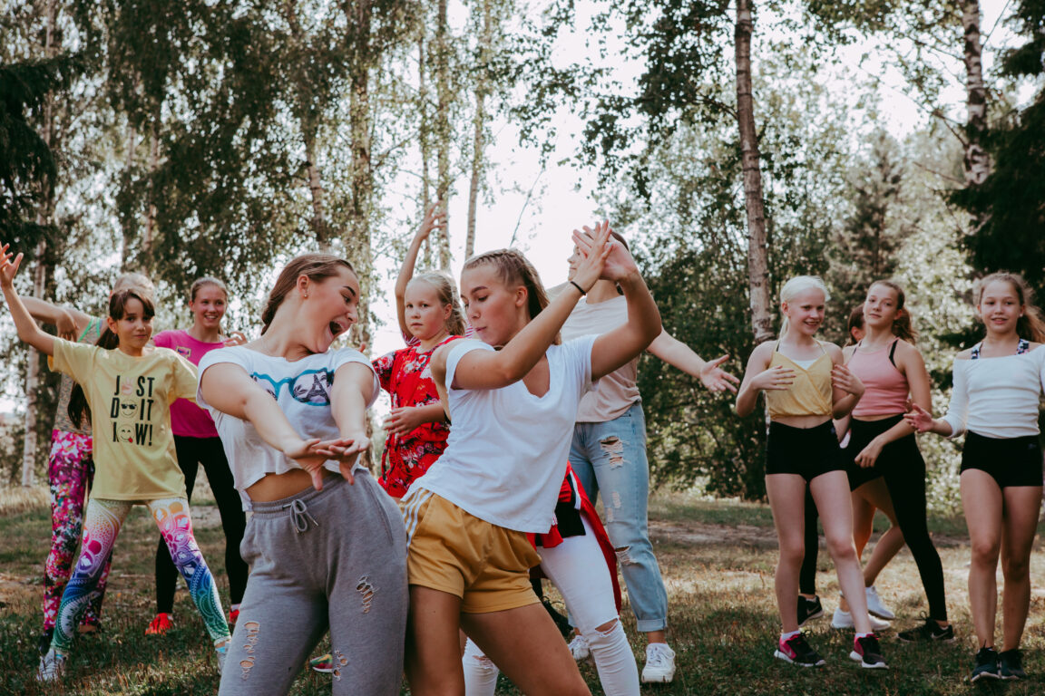 Nuoria ulkona tanssimassa. Kuvan etualalla kaksi nuorta iskevät peput yhteen leikkisästi.