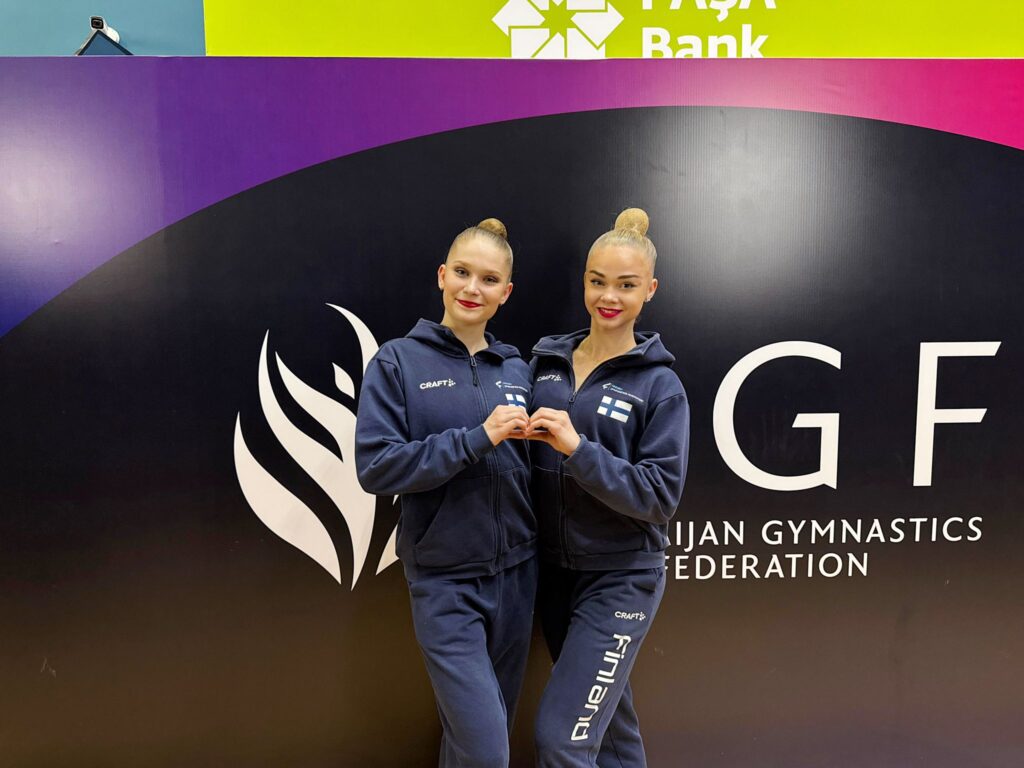 Lia Kallio ja Emmi Piiroinen verryttelyasut päällään näyttävät käsillään sydänmerkkiä.